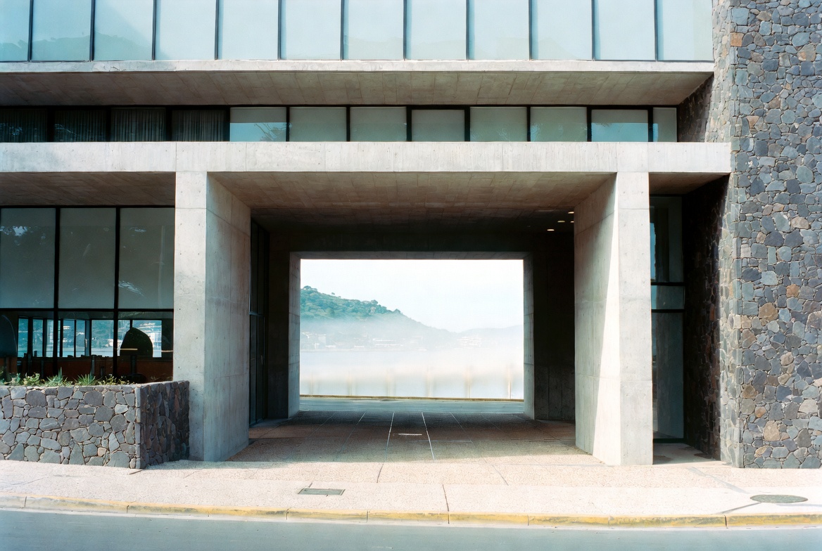 A modern concrete and basalt architectural gateway in Mauritius framing the harbour and hills beyond